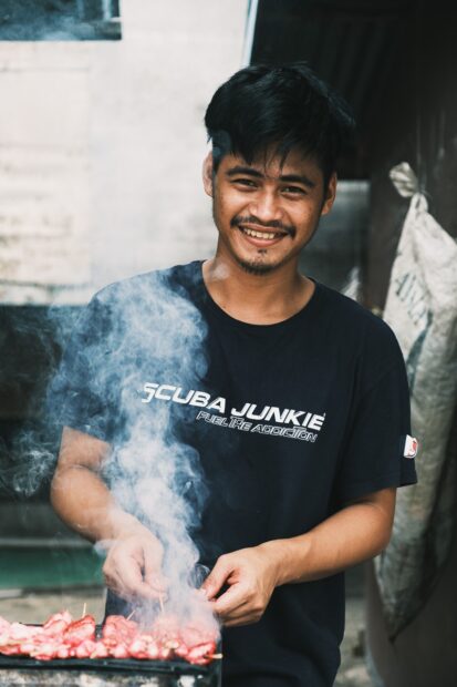 Man smiling while grilling meat on Mabul Island