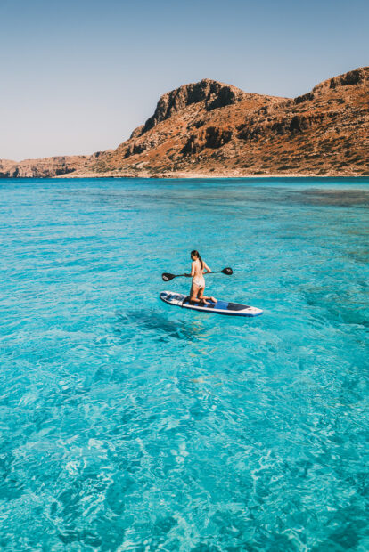 Girl paddle boarding in the crystal clear turquoise water of Balos Beach