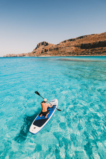 Man paddle boarding in the crystal clear turquoise water of Balos Beach