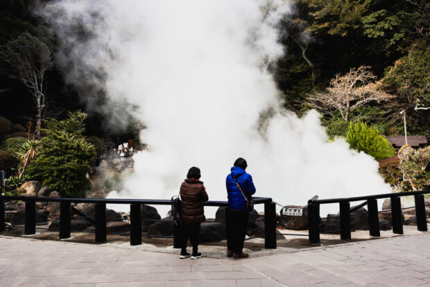 Steam vents rising in front of two people standing at Umi Jigoku Hells of Beppu